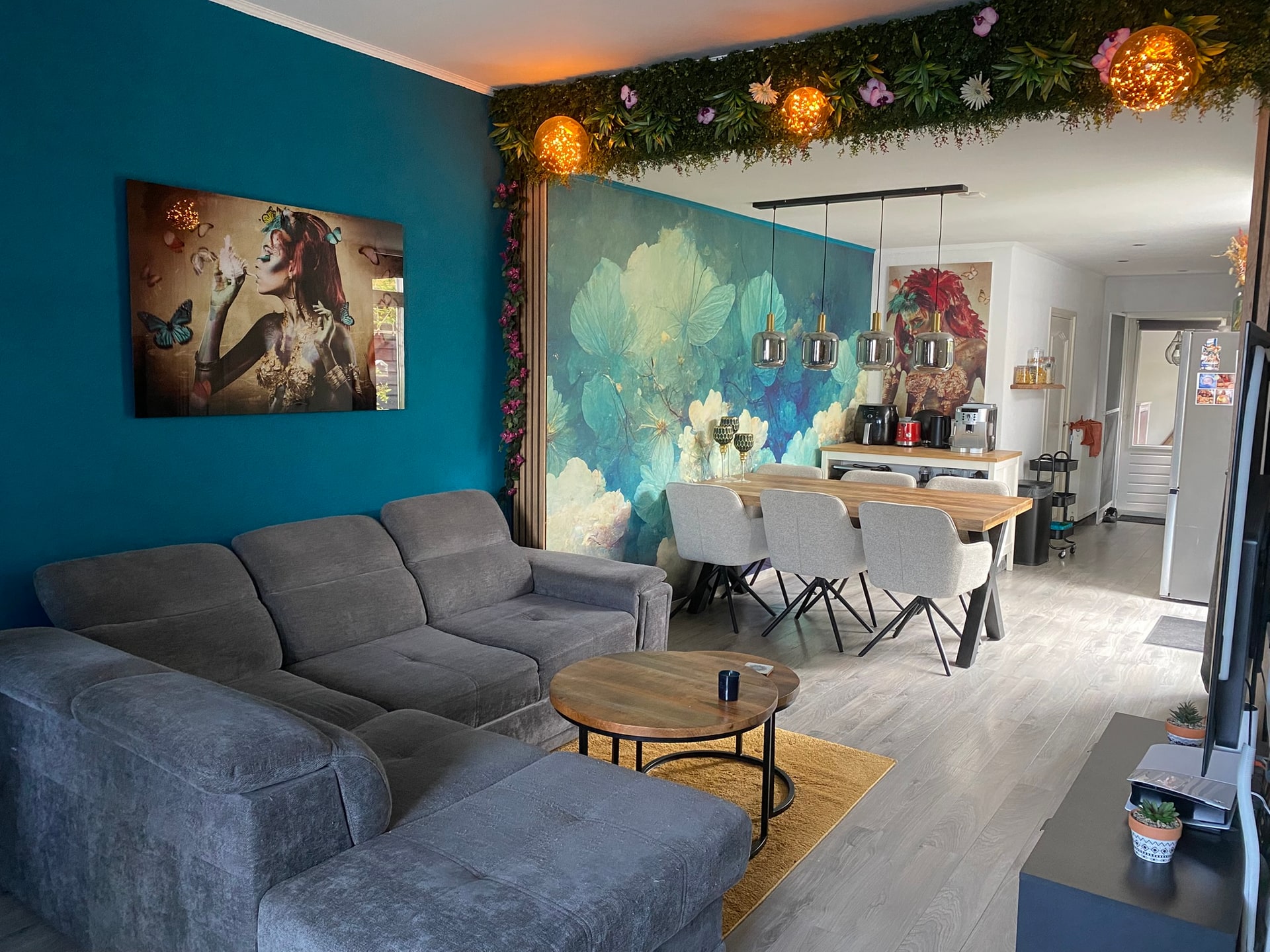 Dezelfde huiskamer bij daglicht, met de petrolblauwe wand en het bloemenbehang